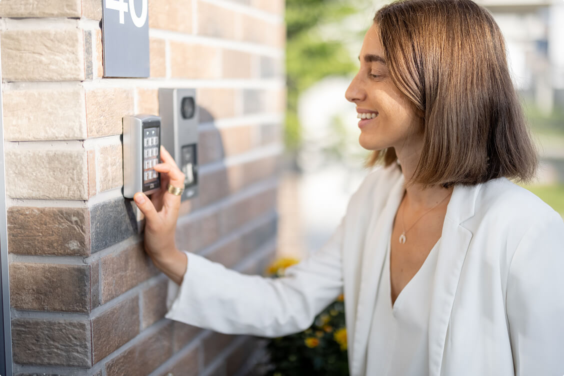 Smiling woman using a security keypad access control system on a brick wall for safe entry.