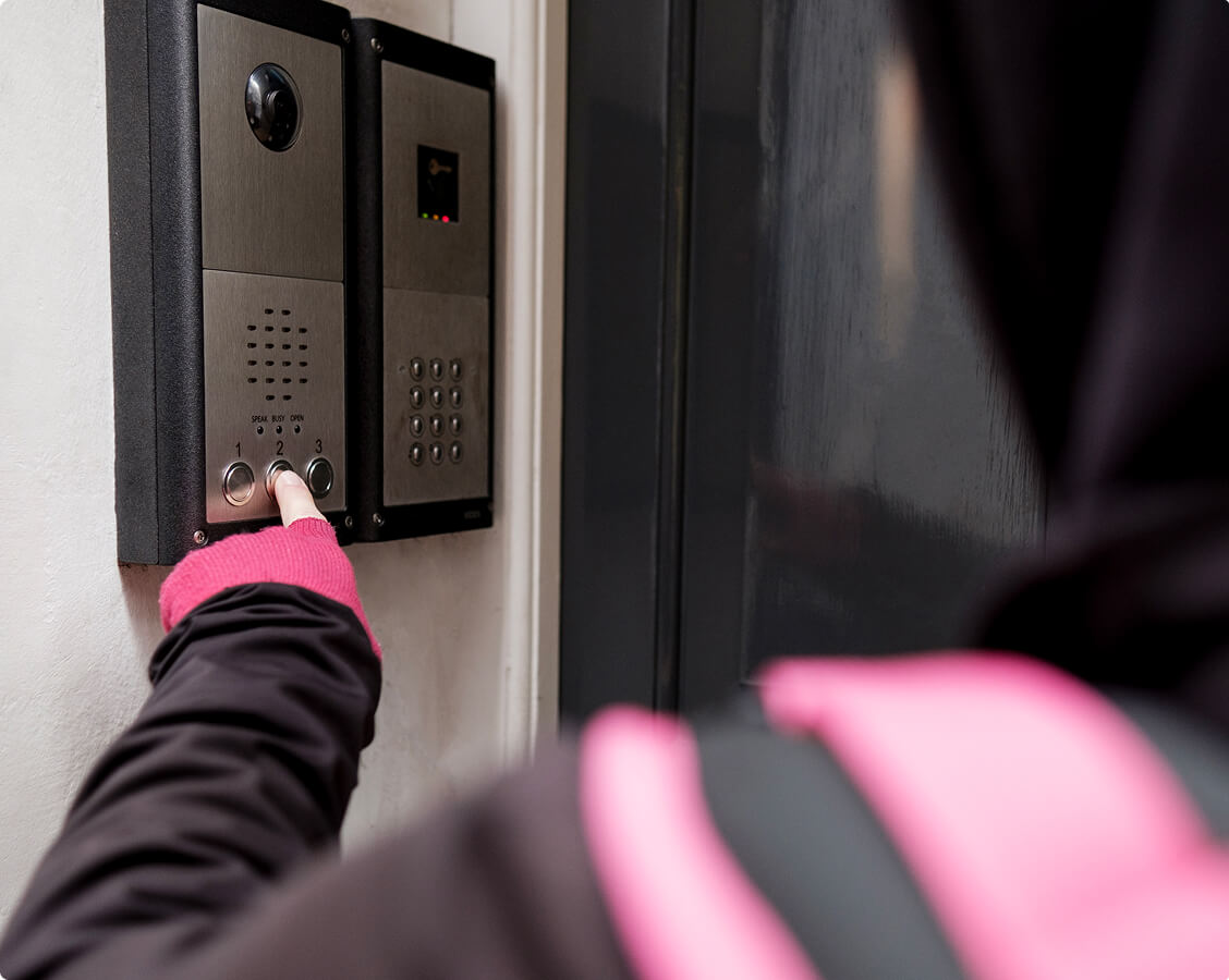Person pressing button on modern intercom and access control system at secure building entrance.